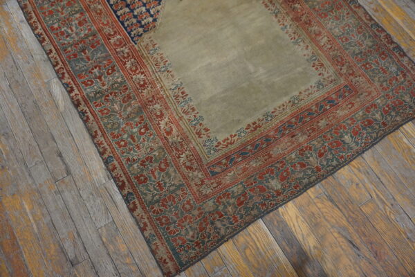 A light green rug with complex red and teal floral borders sits on rustic wood plank flooring.