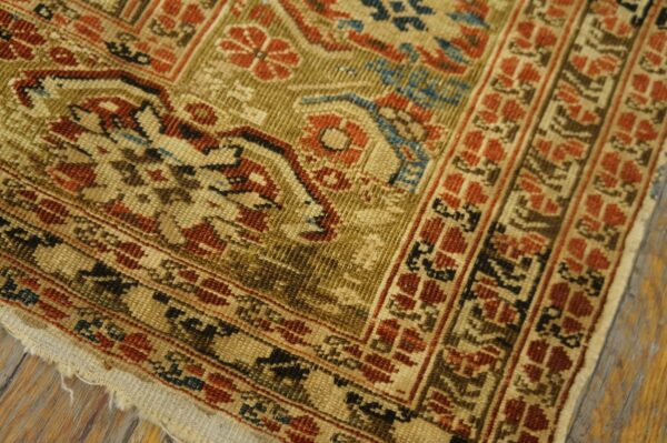 Worn, low-pile rug corner featuring traditional floral and geometric patterns in rust, gold, and blue colors on wood flooring.