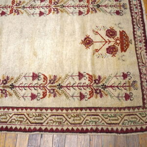 Low-pile cream rug featuring stylized floral and geometric motifs in burgundy and rust on distressed wood flooring.