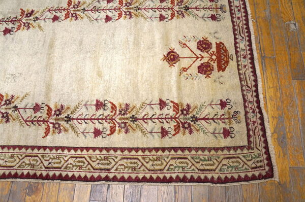 Low-pile cream rug featuring stylized floral and geometric motifs in burgundy and rust on distressed wood flooring.