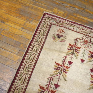 A cream rug with rust and red botanical patterns and a geometric border lies on rustic wooden flooring.