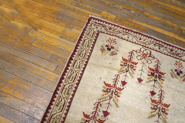A cream rug with rust and red botanical patterns and a geometric border lies on rustic wooden flooring.