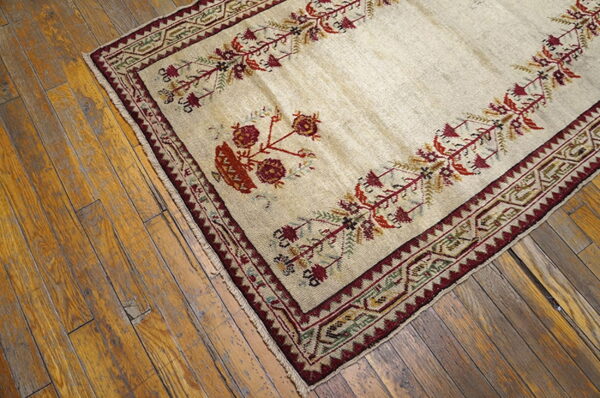 Cream rug with a detailed burgundy floral and vine motif border on rustic wood planks.