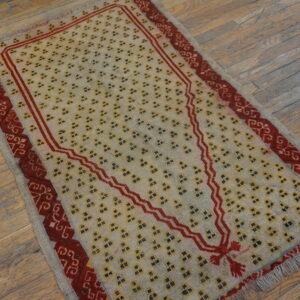 Beige rug with repeating yellow motifs and a prominent red stepped arch rests on distressed wood planks.