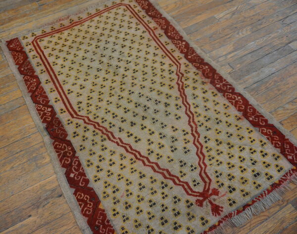 Beige rug with repeating yellow motifs and a prominent red stepped arch rests on distressed wood planks.