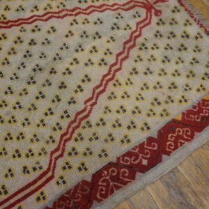 Cream rug with scattered yellow motifs, a red zigzag design, and traditional border on wood planks.