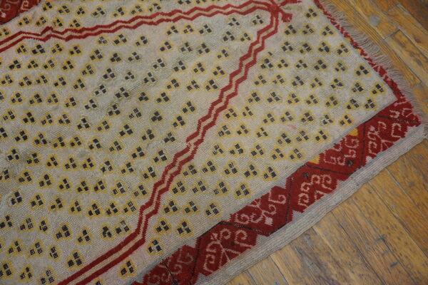 Cream rug with scattered yellow motifs, a red zigzag design, and traditional border on wood planks.