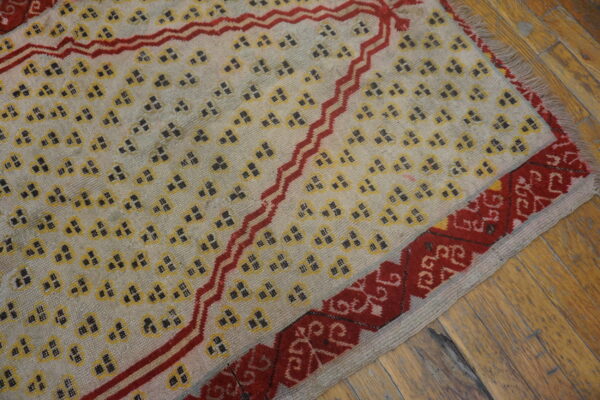 Light rug with repeating yellow and dark geometric symbols, framed by zigzagging and ornate red borders on wood.