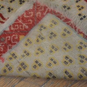 A woven rug with beige, red, yellow, and black geometric patterns folded over wood flooring.