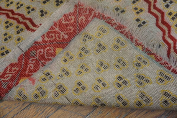 A woven rug with beige, red, yellow, and black geometric patterns folded over wood flooring.