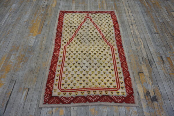 Cream and red rug with geometric motifs and a central arched design on rustic wooden flooring.