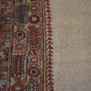 Low-pile beige rug with detailed red, blue, and tan geometric borders shown on gray planks.