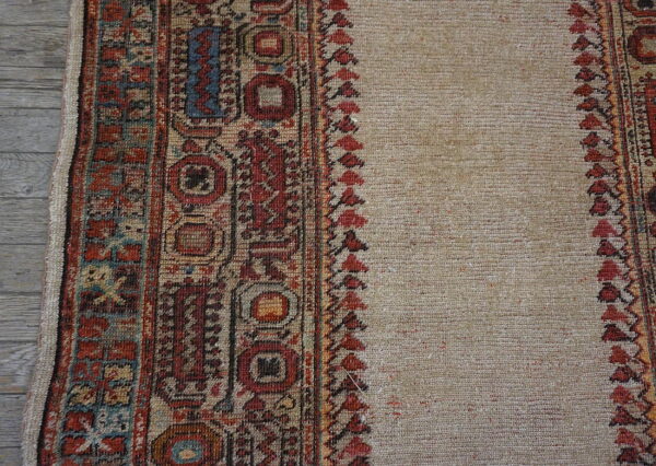 Low-pile beige rug with detailed red, blue, and tan geometric borders shown on gray planks.