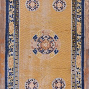 Gold and navy rug featuring a central medallion and four corner motifs, framed by a fret pattern border.