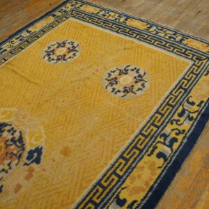 Yellow rug with dark blue geometric borders and large patterned medallions rests on distressed plank flooring.