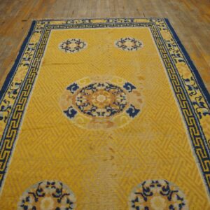 Bright yellow rug with subtle geometric pattern, blue medallions, and a wide navy border on wood floor.