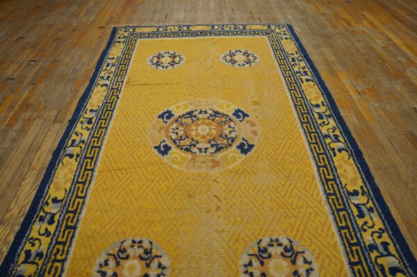 Bright yellow rug with subtle geometric pattern, blue medallions, and a wide navy border on wood floor.