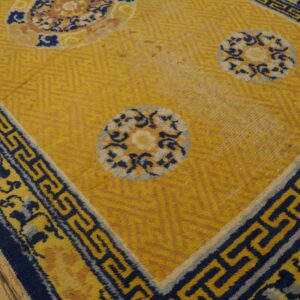 Yellow rug with large blue and tan floral medallions and a wide blue meander border on wood flooring.