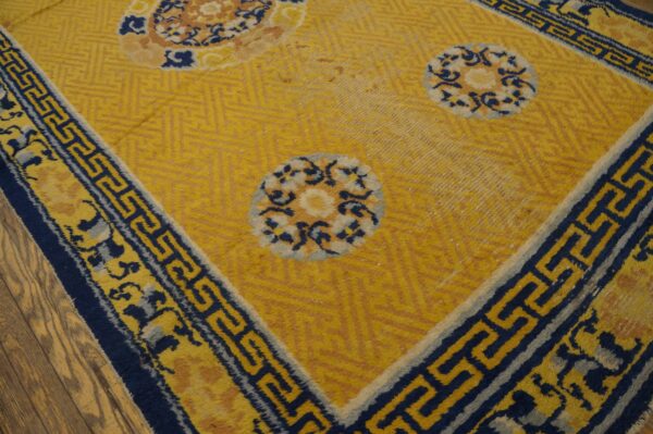 Yellow rug with large blue and tan floral medallions and a wide blue meander border on wood flooring.