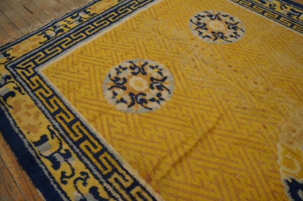 Gold rug with chevron texture and blue and white medallions bordered by a dark blue greek key design.