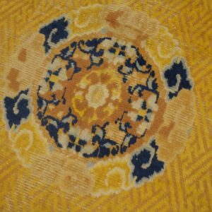 Yellow rug detail showing a central floral medallion in navy, rust, and white against a textured background.
