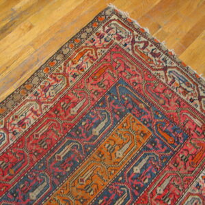 Red, blue, and orange patterned rug corner featuring geometric motifs rests on wood plank flooring.