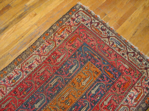 Red, blue, and orange patterned rug corner featuring geometric motifs rests on wood plank flooring.