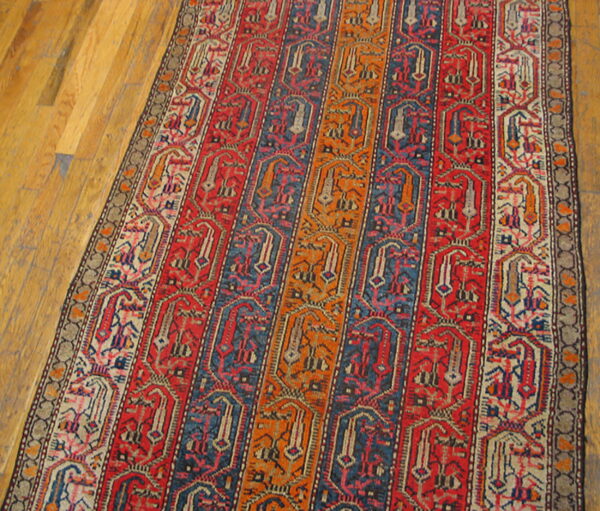 Runner rug with vertical stripes of red, blue, and orange geometric patterns on light hardwood floors.