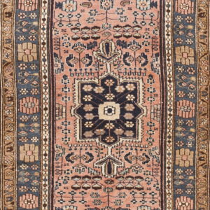 Runner rug with a dusty rose field, a dark central geometric motif, and navy and tan patterned borders.