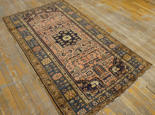 Low-pile rug in coral and navy blue with geometric patterns rests on heavily distressed wooden planks.