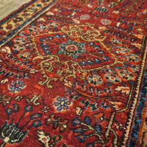 Traditional red runner rug featuring intricate blue and gold floral patterns lies across light wood flooring.