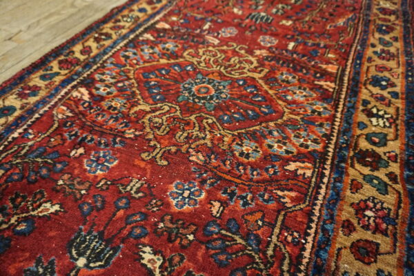 Traditional red runner rug featuring intricate blue and gold floral patterns lies across light wood flooring.