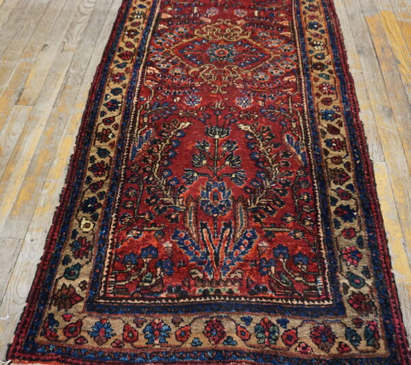 A burgundy runner rug featuring a complex floral medallion design with blue and tan motifs rests on distressed wood floors.