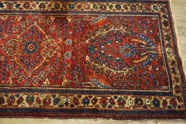 The high-detail red rug displays intricate blue and beige floral motifs and decorative borders on wood planks.