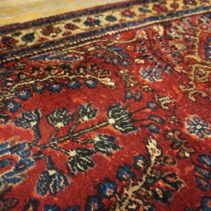 Detailed view of a deep red traditional rug with blue and tan patterns on golden wood flooring.