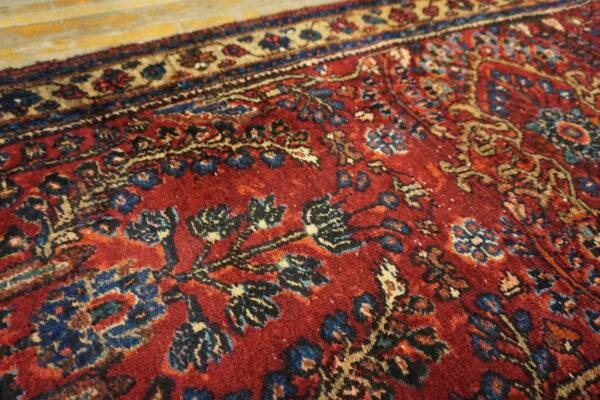 Detailed view of a deep red traditional rug with blue and tan patterns on golden wood flooring.