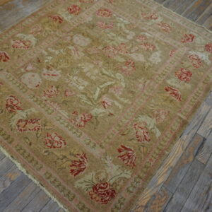 Tan, red, and pink floral square rug lying on distressed gray wood plank flooring.