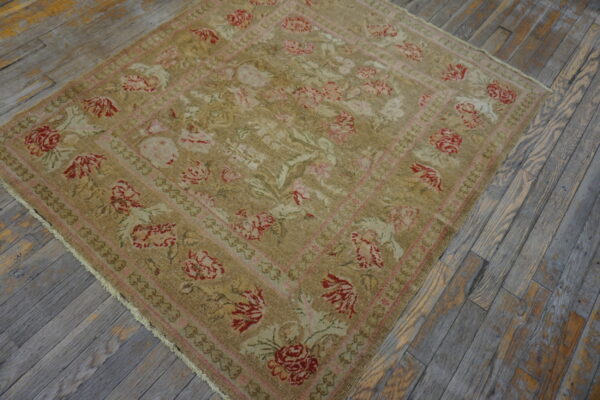 Tan, red, and pink floral square rug lying on distressed gray wood plank flooring.