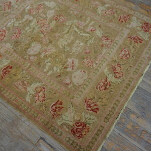 Tan rug with a traditional red and pink floral design and multiple borders on distressed gray flooring.