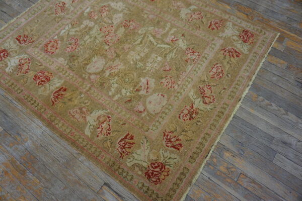 Tan rug with a traditional red and pink floral design and multiple borders on distressed gray flooring.