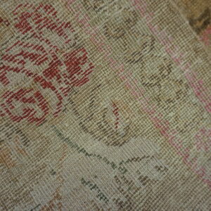 Detailed view of a low-pile rug showing distressed beige texture with red, pink, and brown patterns.