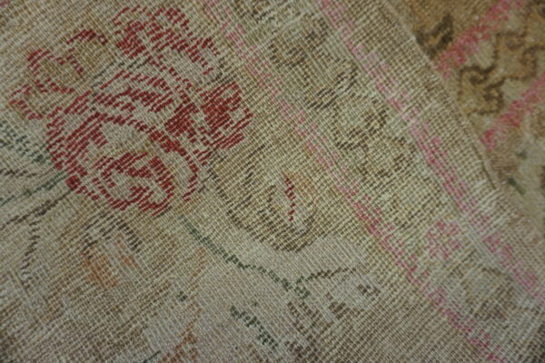 Detailed view of a low-pile rug showing distressed beige texture with red, pink, and brown patterns.