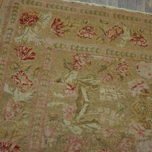Muted khaki rug featuring elaborate red and pink floral motifs bordered by scrollwork on distressed wood.