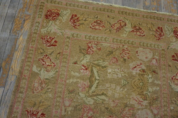 Muted khaki rug featuring elaborate red and pink floral motifs bordered by scrollwork on distressed wood.