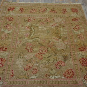 Low-pile, distressed tan rug featuring large red and pink floral designs on weathered gray wood floor.