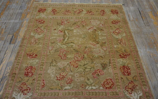 Low-pile, distressed tan rug featuring large red and pink floral designs on weathered gray wood floor.