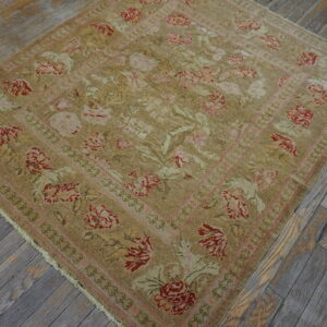 A beige rug with a faded floral pattern in red and pink rests on distressed gray wood floors.