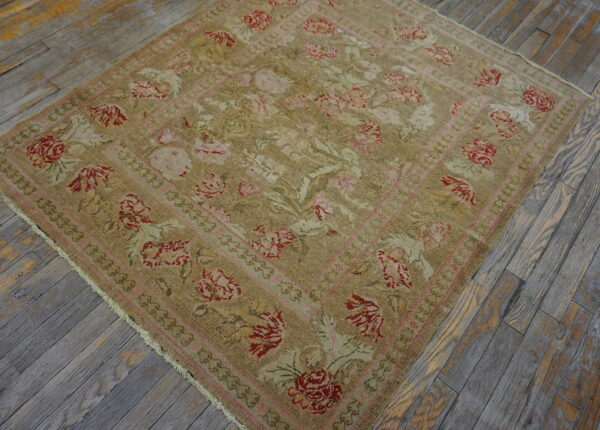 A beige rug with a faded floral pattern in red and pink rests on distressed gray wood floors.