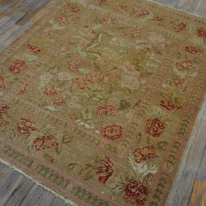 Low-pile tan rug with fading red and pink floral patterns rests on weathered gray wood flooring.