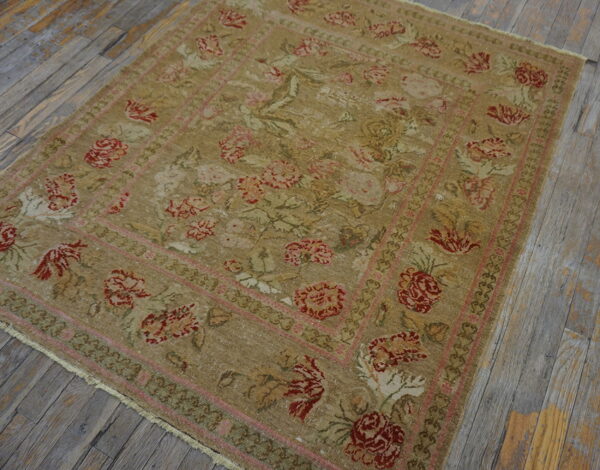 Low-pile tan rug with fading red and pink floral patterns rests on weathered gray wood flooring.
